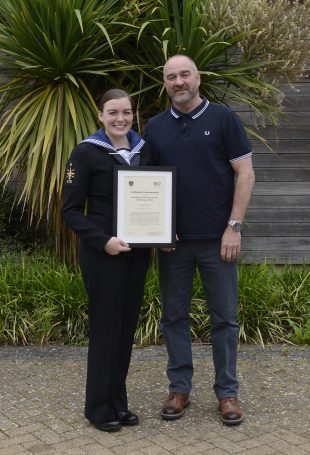 A picture showing ET Chelcie Evans holding her framed ISS Chief Executive Officer’s commendation, alongside her Father