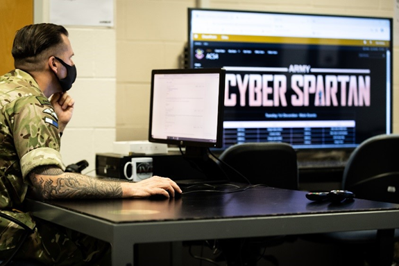 An image showing a military person working at a computer. A screen in the background shows the words 'Cyber Spartan'